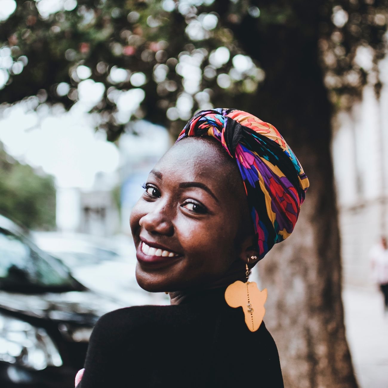 Beautiful portrait of a smiling African woman wearing a vibrant headscarf and earring outdoors in an urban setting.